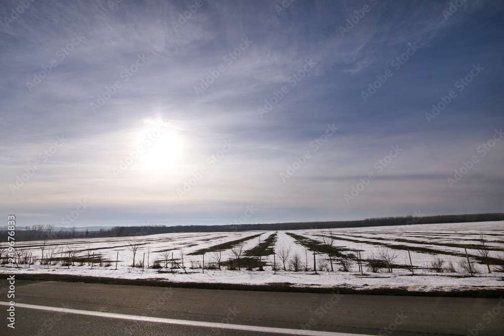 View from highway of winter landscape meadows and fields covered with layer of snow. Amazing natural environment with blue sky and sun. Beautiful landscape covered in snow in winter, seasons specific.
