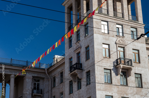 Decorative pommel buildings in the style of the Stalin Empire style and the facade of the building of natural stone. Festive colored flags. St. Petersburg. Russia, Narva Square, May 9, 2018 photo