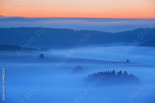 Sunset Over Misty Landscape Scenic View Of Foggy Morning Sky With Rising Sun Above dreamy Forest. Mountain range with visible silhouettes through the morning colorful fog Beautiful background concept