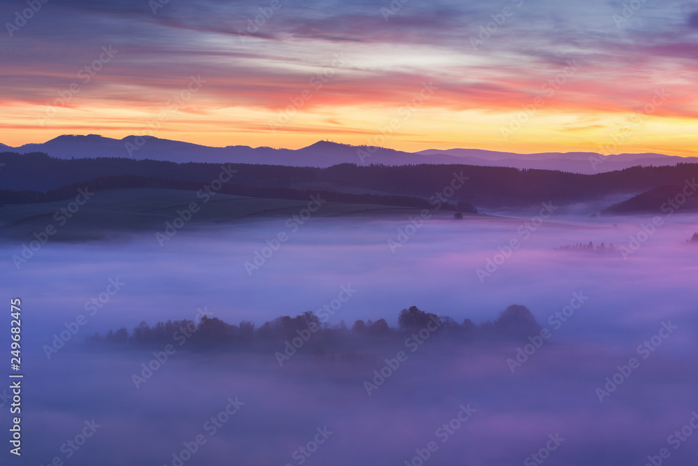 Sunset Over Misty Landscape Scenic View Of Foggy Morning Sky With Rising Sun Above dreamy Forest. Mountain range with visible silhouettes through the morning colorful fog  Beautiful background concept
