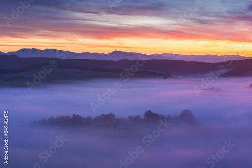 Sunset Over Misty Landscape Scenic View Of Foggy Morning Sky With Rising Sun Above dreamy Forest. Mountain range with visible silhouettes through the morning colorful fog  Beautiful background concept © Michal