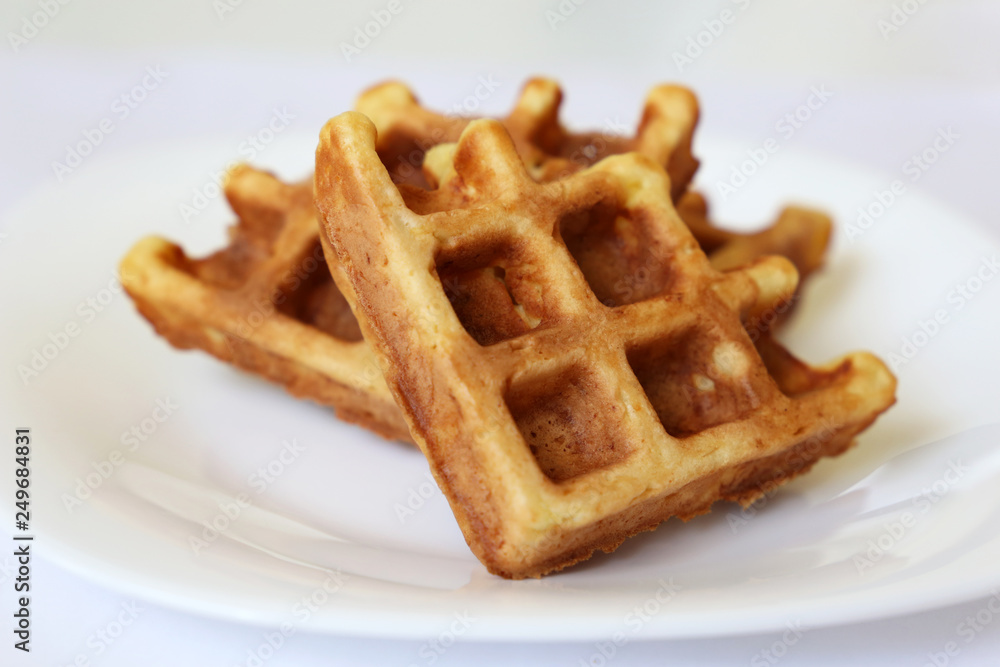 Belgian waffles in white plate. Healthy breakfast close up, pieces of freshly baked classic wafer Belgian waffles in white plate. Healthy breakfast close up, pieces of freshly baked classic wafer