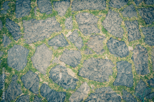Cobblestone pavement background with copy space. Abstract old close-up cobble stone texture. Paving stone patterned street view from above, paving tiles with grass.
