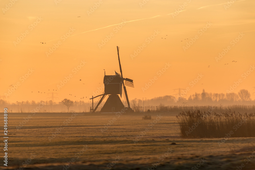 Orange morning sky over a historic Dutch windmill on a foggy horizon in the countryside 