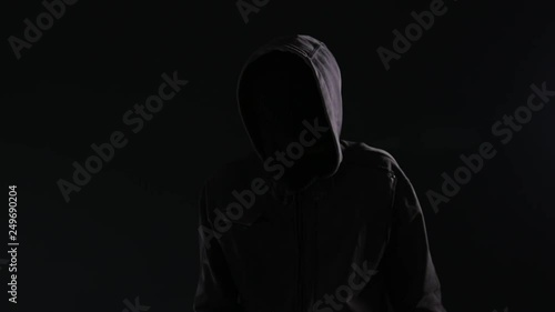 Unrecognizable hooded maniac stalker gesturing finger on lips or shh sign to silence the victim of his crime act