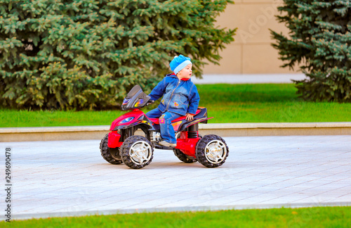 Funny little boy rides an electric red car in the city park