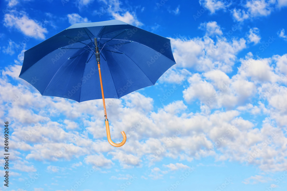 Wind of change concept.Blue umbrella flies in sky against of white clouds.