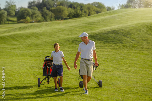 Boy and man golfers walking on golf course with carts