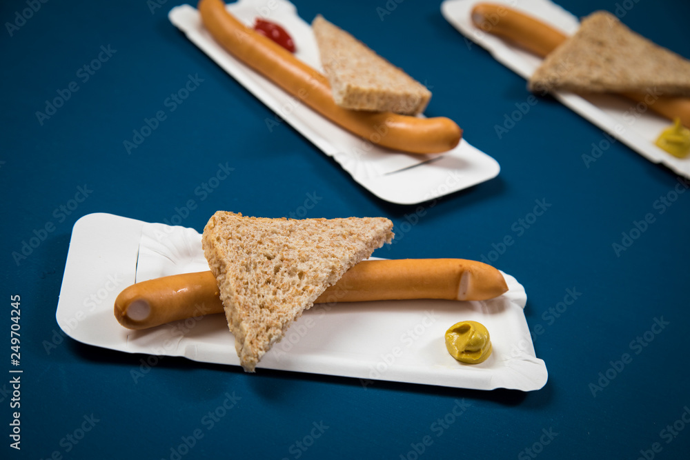 Fototapeta premium Wiener Würstchen mit Vollkorn Brot Scheibe auf Einweg Pappteller mit Senf und Ketchup auf Hintergrund Blau