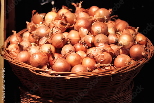 Large bulbs of onions. Many onions in a large wicker basket. Vegetables for a healthy diet. Basket with onions on black background. Onion for a healthy diet.