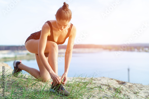 Fotografie A beautiful young Caucasian girl athlete on a morning jog stopped to rest to declare the laces on the running shoes