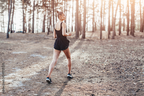 Young caucasian girl on a morning run in a pine forest. Exercises in nature and a healthy lifestyle