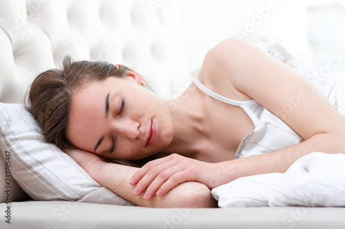 Young beautiful caucasian woman covered with a blanket sleeping and relaxing on the pillow in bed in early morning. Girl resting with closed eyes in bedroom at home