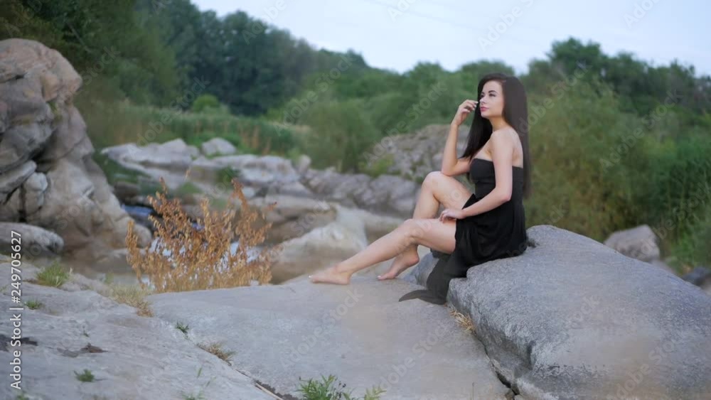 Beautiful brunette girl with long hair sitting on the big stone, she looks off into the distance. Beautiful brunette girl with long hair sitting on the big stone, she looks off into the distance.