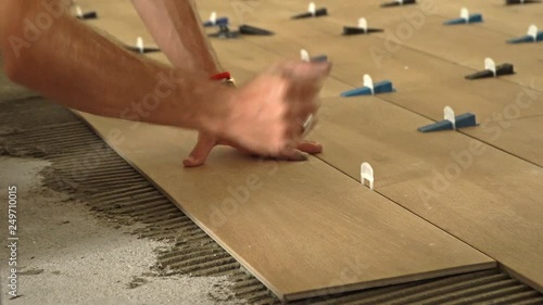 Hands of a professional tiler laying down new tile on tile mortar on the floor