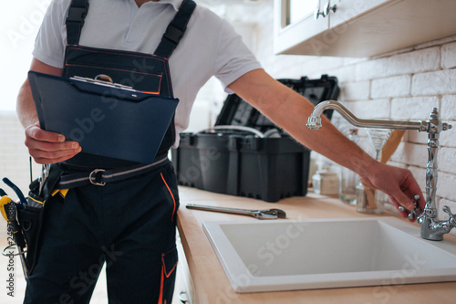 Cut view of handyman holding tool box and wrench in hands. He stand in kitchen at sink. He open water tap.