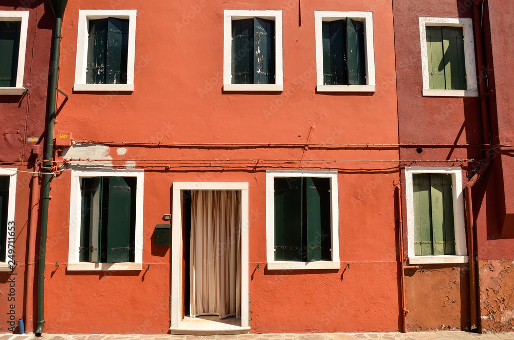 Green window with shutters in Mediterranean style on red wall.  Colorful houses in Burano island near Venice, Italy