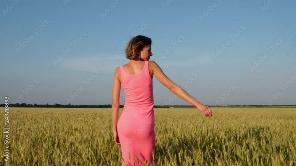A young beautiful woman dance, in a golden field of wheat at sunset. Shot from behind. A young beautiful woman dance, in a golden field of wheat at sunset. Shot from behind.