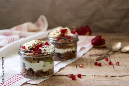 Granola with yogurt and fruit in glass jars on a wooden table. Rustic style.
