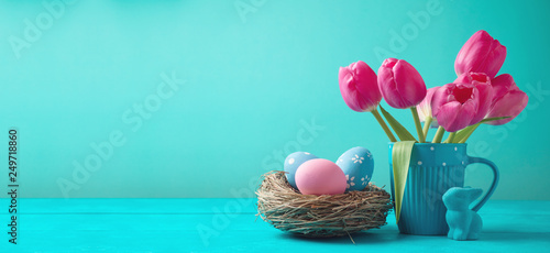 Easter holiday background with tulip flowers, eggs decoration in bird nest and bunny on wooden blue table