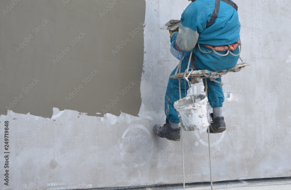 builder in winter hanging on a rope repairing a wall the face is not visible builder in winter hanging on a rope repairing a wall the face is not visible