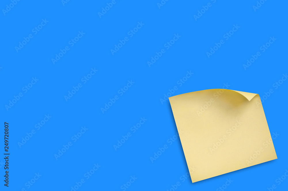 One blank square yellow sticker with curved corner attached on blue table in office or fridge in home. Top view. Copy space for your text. Business or education concept One blank square yellow sticker with curved corner attached on blue table in office or fridge in home. Top view. Copy space for your text. Business or education concept