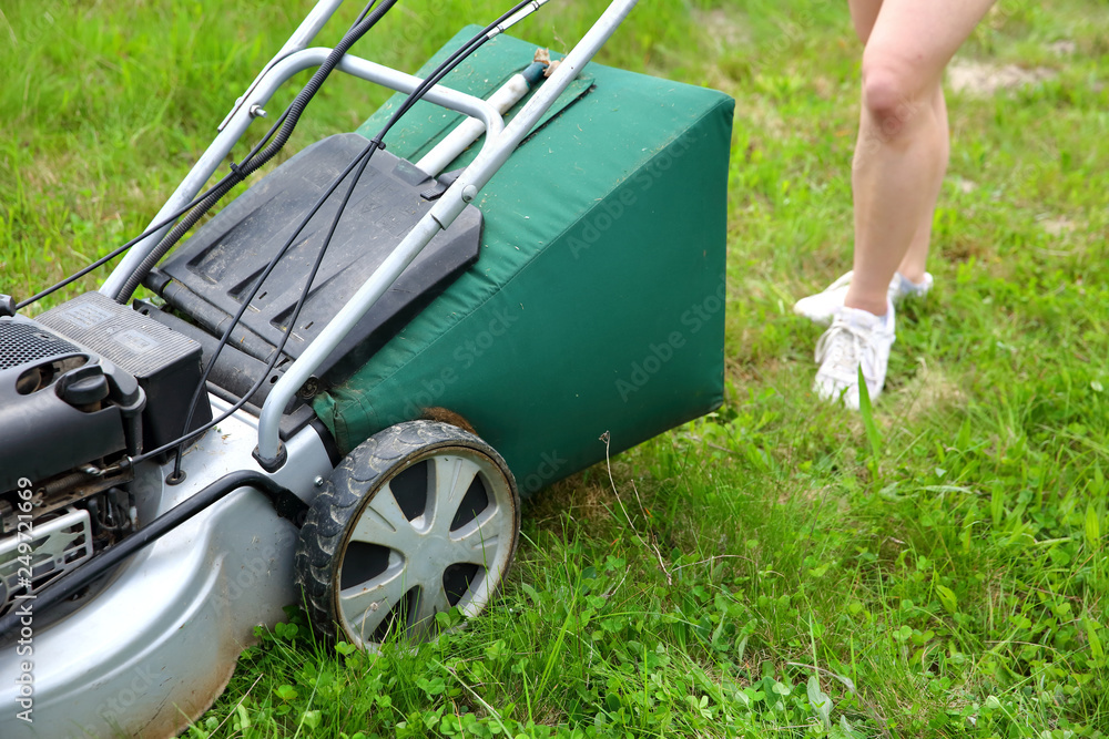 Fototapeta premium Teenage girl pruning green high grass with the help of an petrol lawn mower.