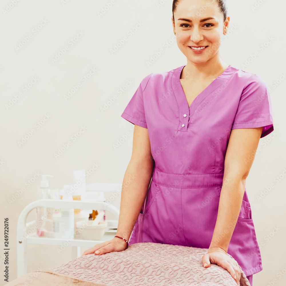 Portrait of young attractive masseur posing near massage table in spa salon Portrait of young attractive masseur posing near massage table in spa salon