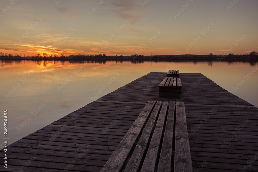 Wooden bridge with planks and sunset over a calm lake