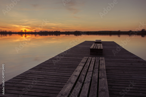 Fototapeta Naklejka Na Ścianę i Meble -  Wooden bridge with planks and sunset over a calm lake