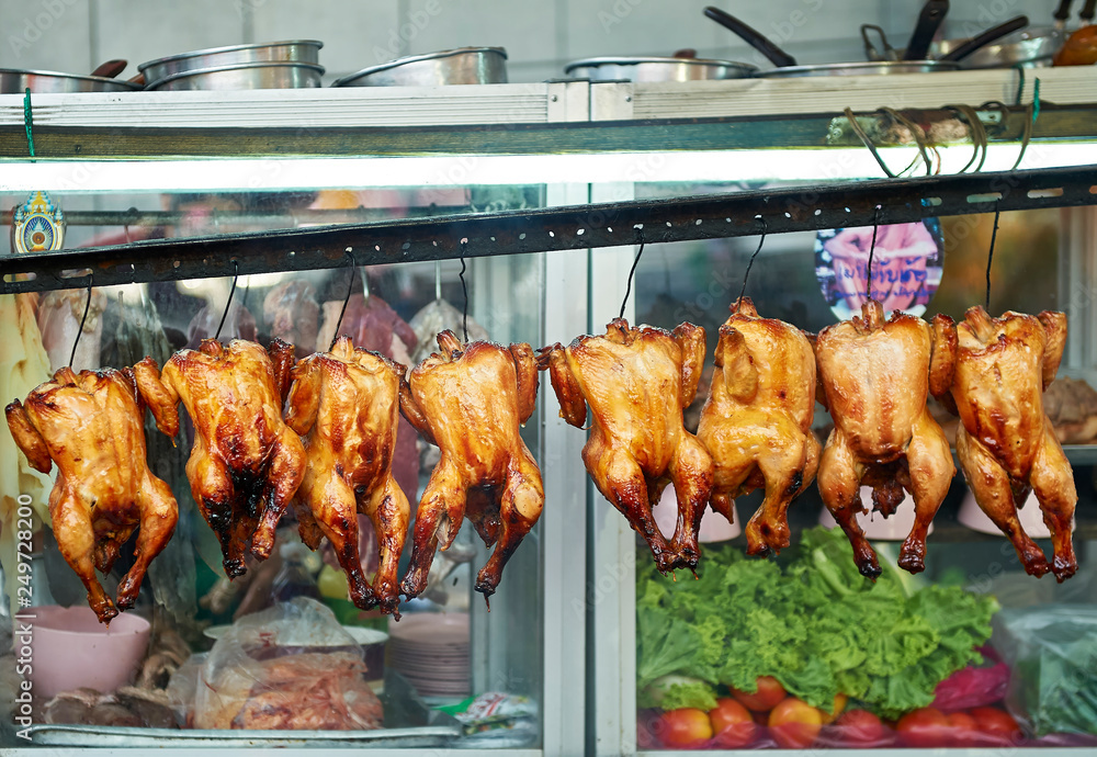 Whole grilled chicken hanging in line at a small street restaurant