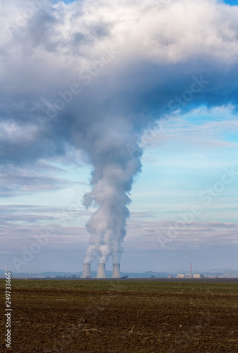 Cooling towers of nuclear power plant (NPP) Jaslovske Bohunice (EBO) in Slovakia. Clouds of thick smoke from chimneys on blue sky at winter day. Cooling towers of power plant with water steam.