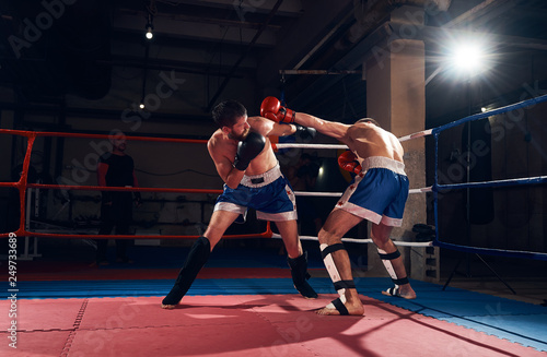 Two attractive sportsmen boxers practicing kickboxing, fighting in the ring at the sport club