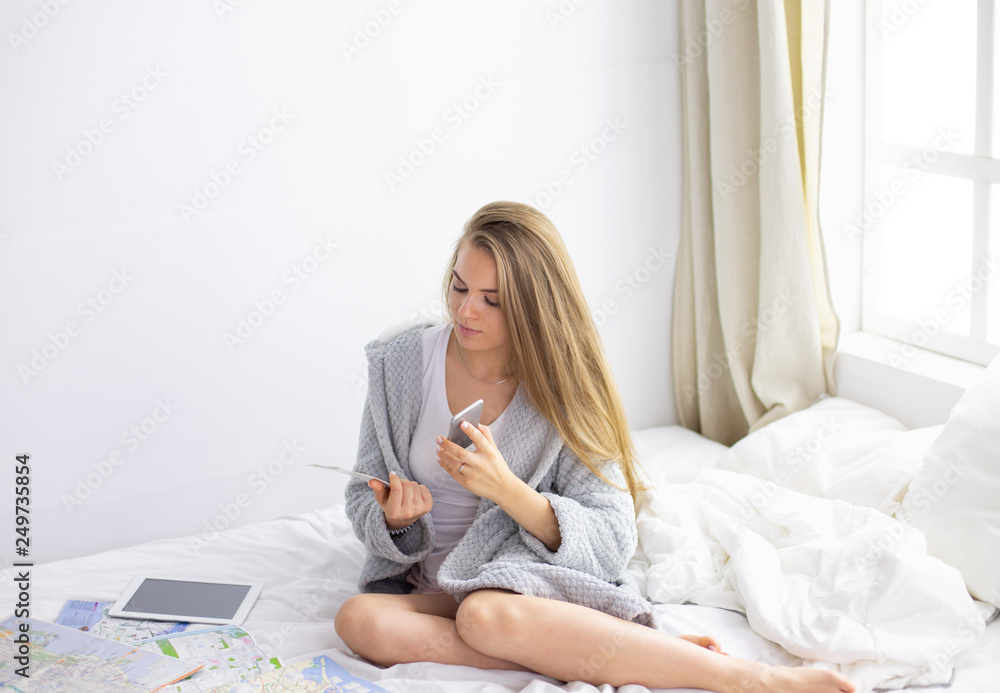 Happy young girl in bed using phone, tablet and maps to search for travel Happy young girl in bed using phone, tablet and maps to search for travel