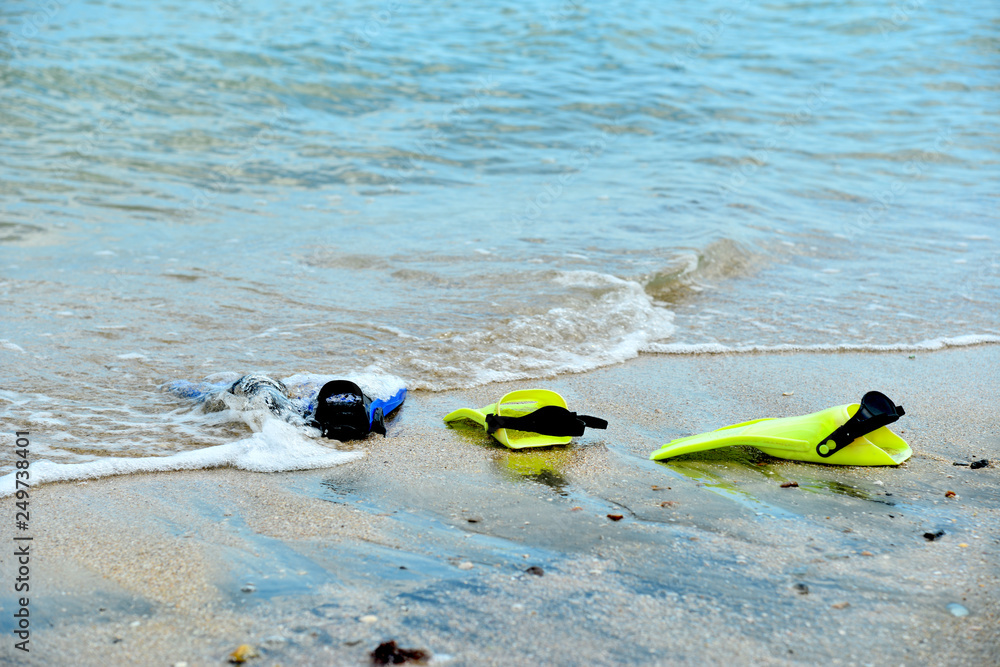 Naklejka premium Yellow and blue flippers for diving lie on the beach in the water.