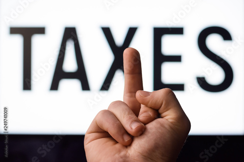 Angry man showing middle finger to screen with inscription TAXES having no desire to pay taxes