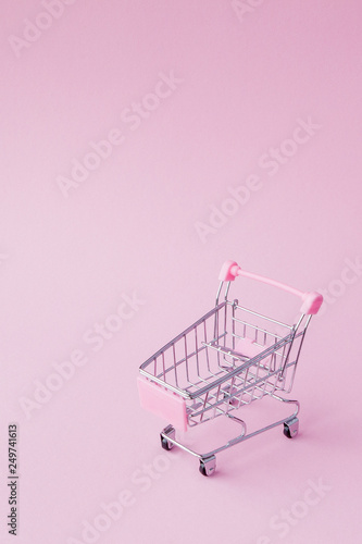 Small supermarket grocery push cart for shopping toy with wheels and pink plastic elements on pink pastel color paper flat lay background. Concept of shopping. Copy space for advertisement