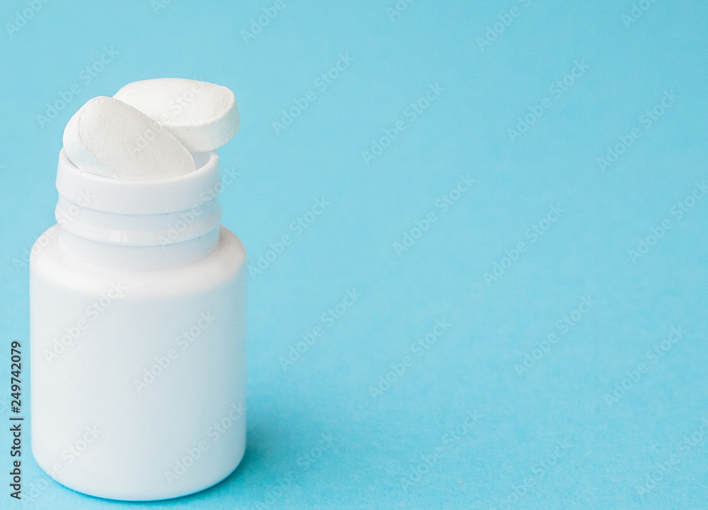 Close up pills spilling out of pill bottle on blue background. Medicine, medical insurance or pharmacy concept Close up pills spilling out of pill bottle on blue background. Medicine, medical insurance or pharmacy concept