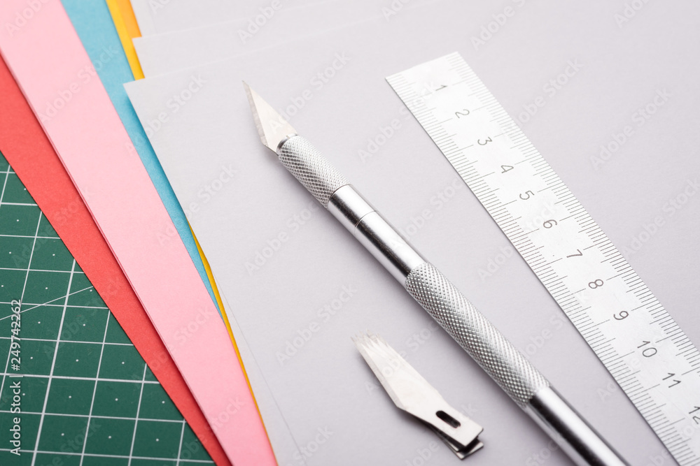 Professional scalpel, ruler and set of sharp blades on papers of different colour on cutting mat Professional scalpel, ruler and set of sharp blades on papers of different colour on cutting mat