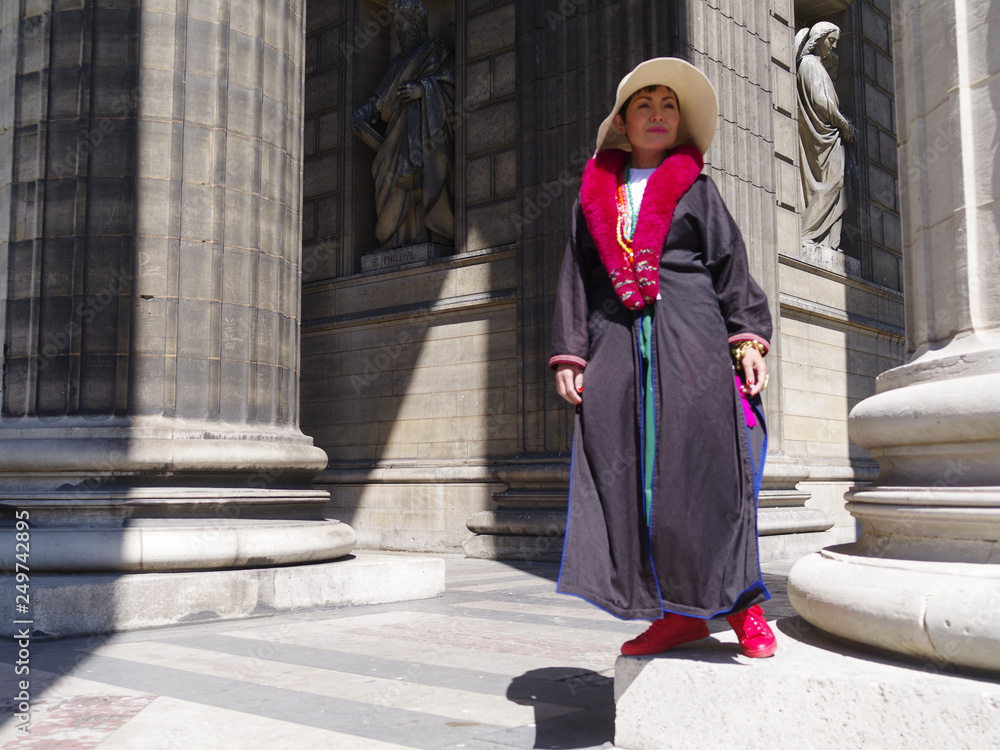Femme avec un mateau noir et une écharpe rouge posant devant les colonnes de l'église de la Madeleine à Paris