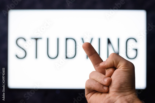 Learner with European appearance showing middle finger to a screen with inscription STUDYING. Student being bored of studying decides to give it up.