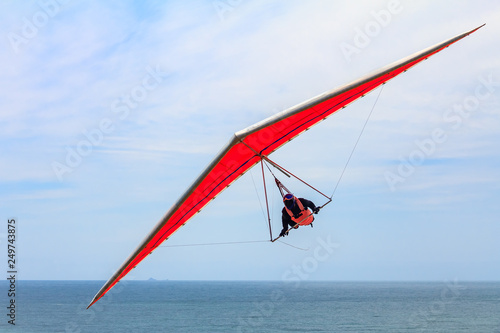 Hang gliding man flying on an orange wing at Fort Funston in San Francisco, one of the premier hang-gliding spots in the country