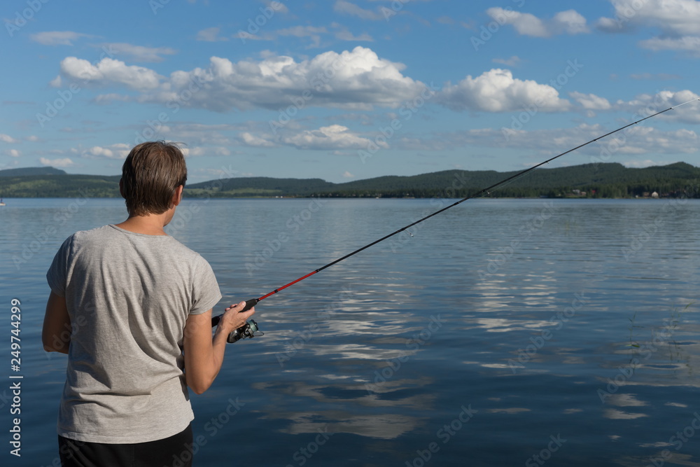 Woman is fishing from a beautiful blue lake against a mountainous shore and the sky with clouds. Natural shot. Woman is fishing from a beautiful blue lake against a mountainous shore and the sky with clouds. Natural shot.