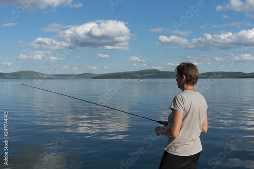 A woman fisherman catches fish for a bait from a blue lake on the background of a mountainous coast. Natural shot.