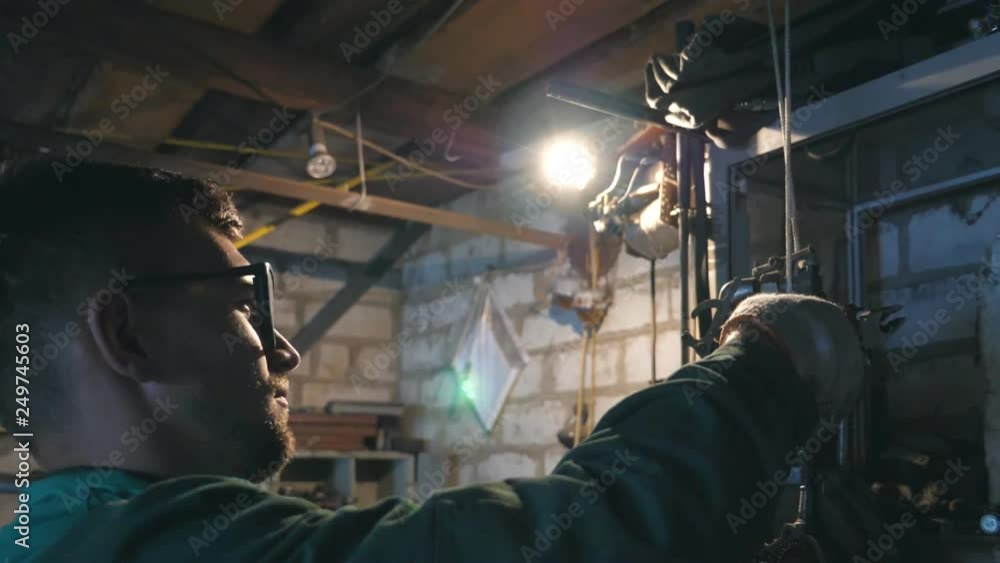 Mechanic doing his work using tool. Man in workwear works in garage or workshop. Profile of young male repairer in glasses. Hard work concept. Dolly shot Slow motion Close up Mechanic doing his work using tool. Man in workwear works in garage or workshop. Profile of young male repairer in glasses. Hard work concept. Dolly shot Slow motion Close up