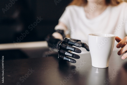 disabled girl controlling her actitions, close up cropped photo. artificial fingers touching the cup on the table, sensorics concept photo