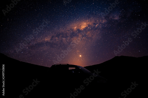 Silhouette car and orange Milky way rising over the peak of mountain.