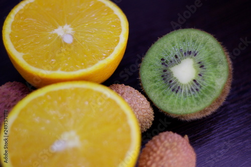 still life of citrus, juicy kiwi and orange in the cut and Litchi chinensis on a dark background