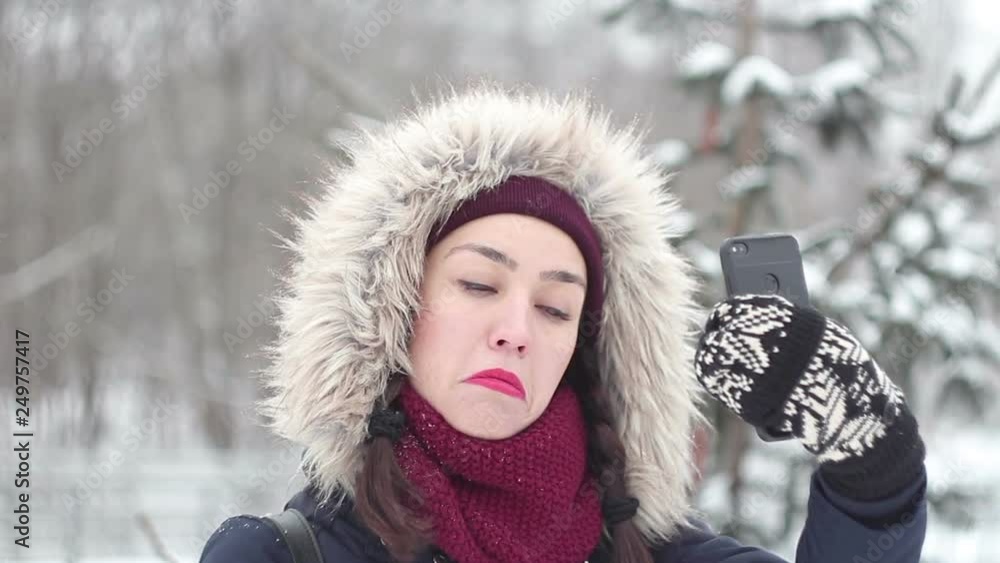 Young beautiful girl makes selfie on her smartphone while walking in a winter park.Portrait. Young beautiful girl makes selfie on her smartphone while walking in a winter park.Portrait.