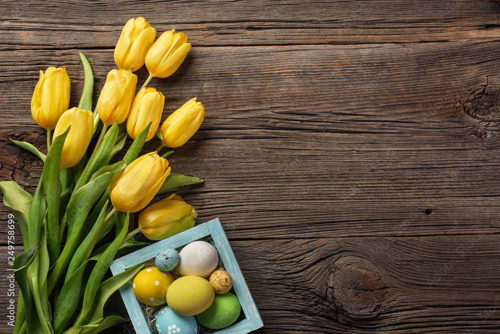 Yellow tulips in a paper bag, a nest with Easter eggs on a wooden background. Top view with copy space